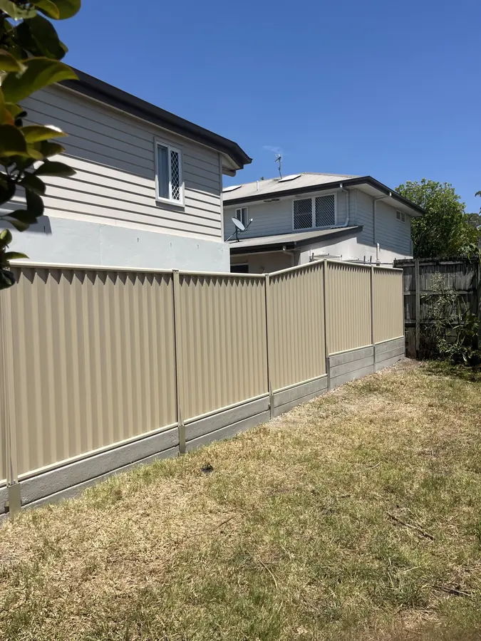 Cream Colorbond fence with a castellated picket top on a concrete sleeper plinth