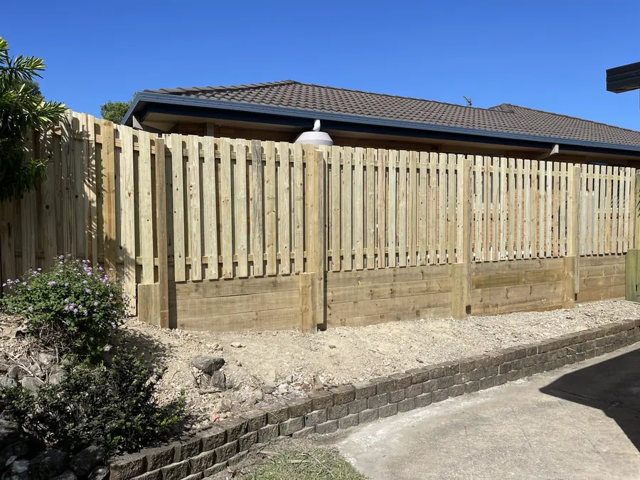 Spaced paling timber fence stepped over a treated pine sleeper retaining wall