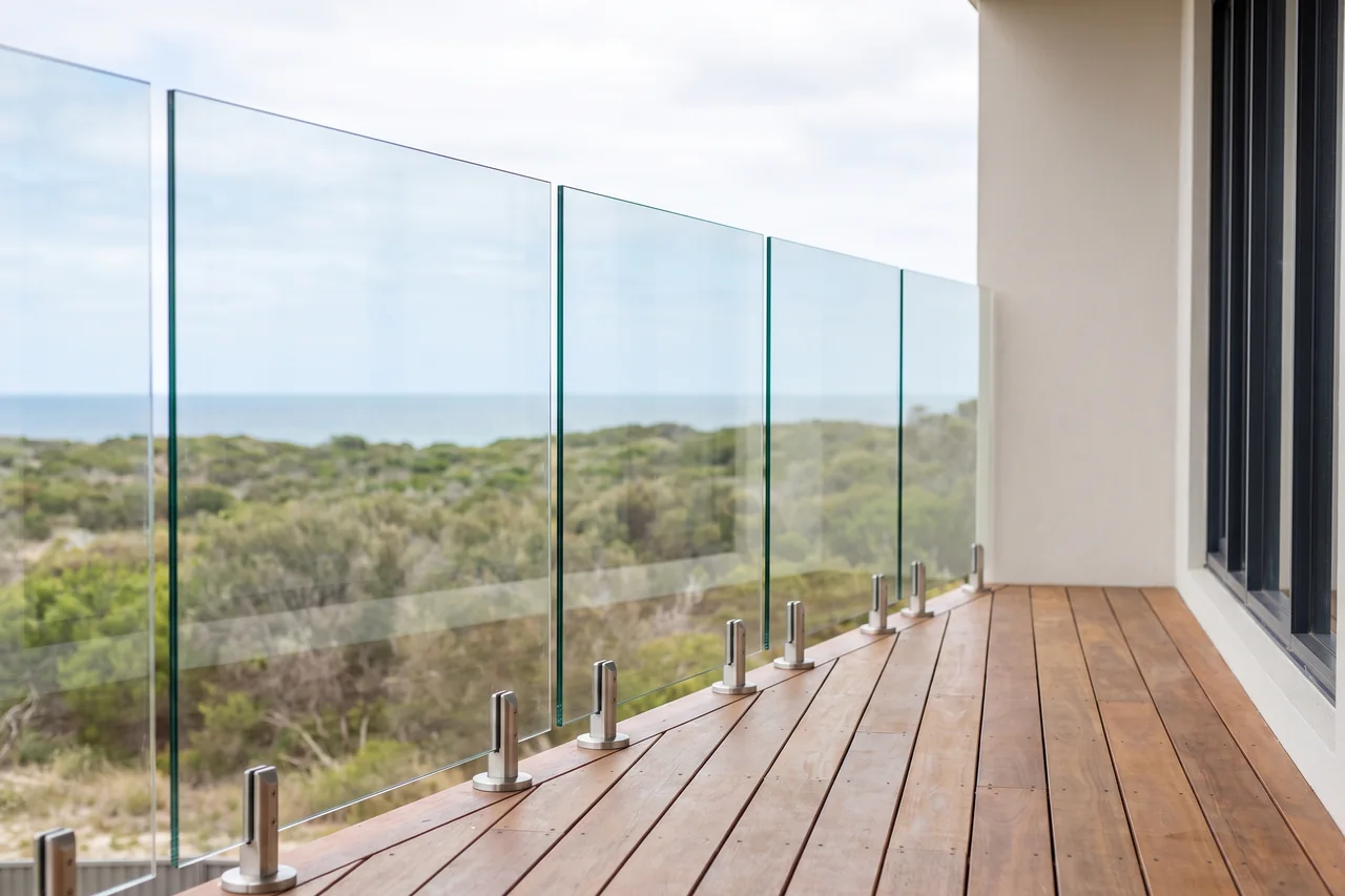 Frameless glass balustrade on a coastal timber deck, fixed on brushed stainless spigots with no top rail